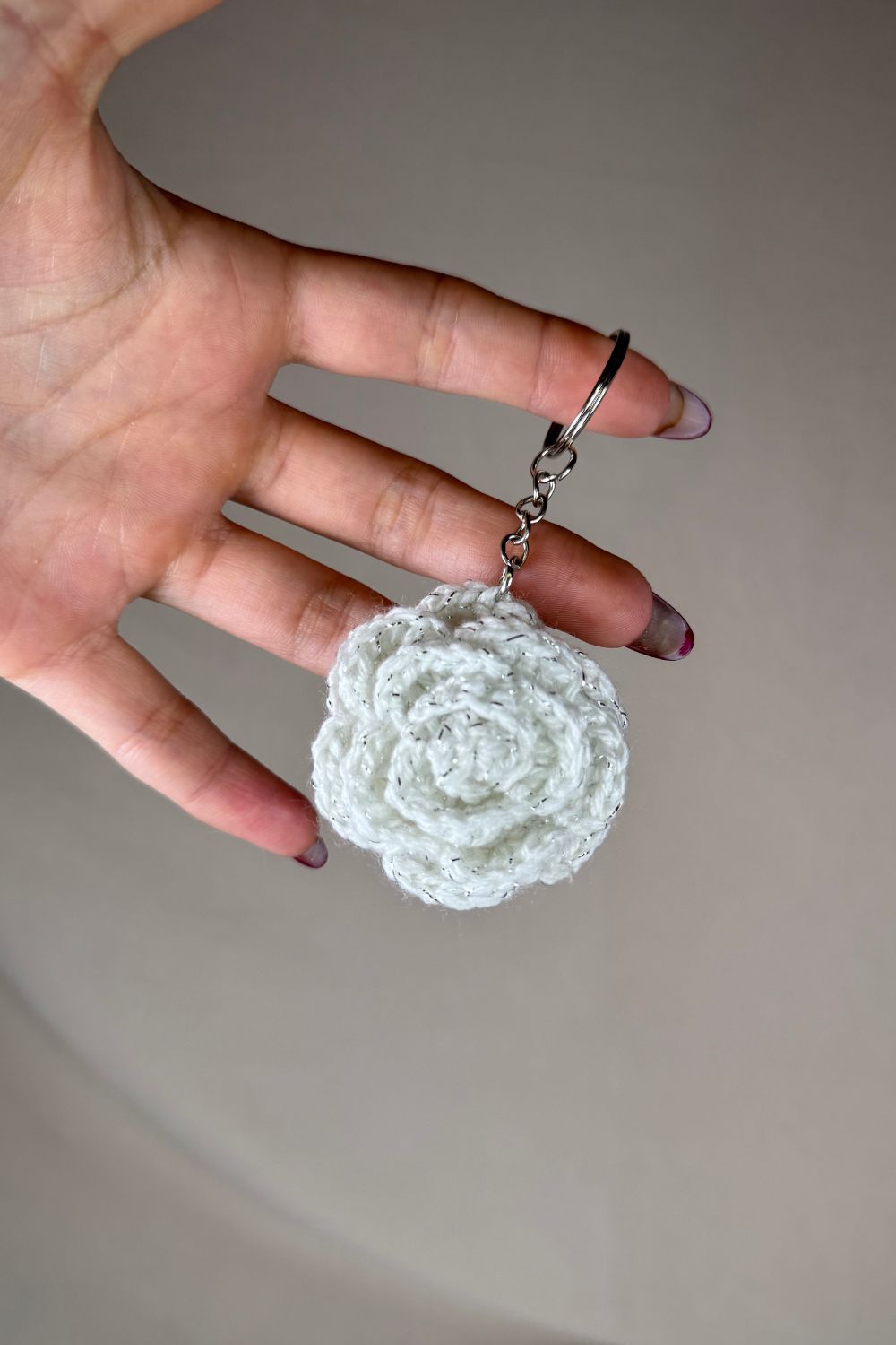 Portachiavi con rosa bianca fatto a mano in Italia da Made By Hand, creazione artigianale in miniatura con fiore rosa all’uncinetto, mostrato in mano per evidenziare i dettagli e le dimensioni