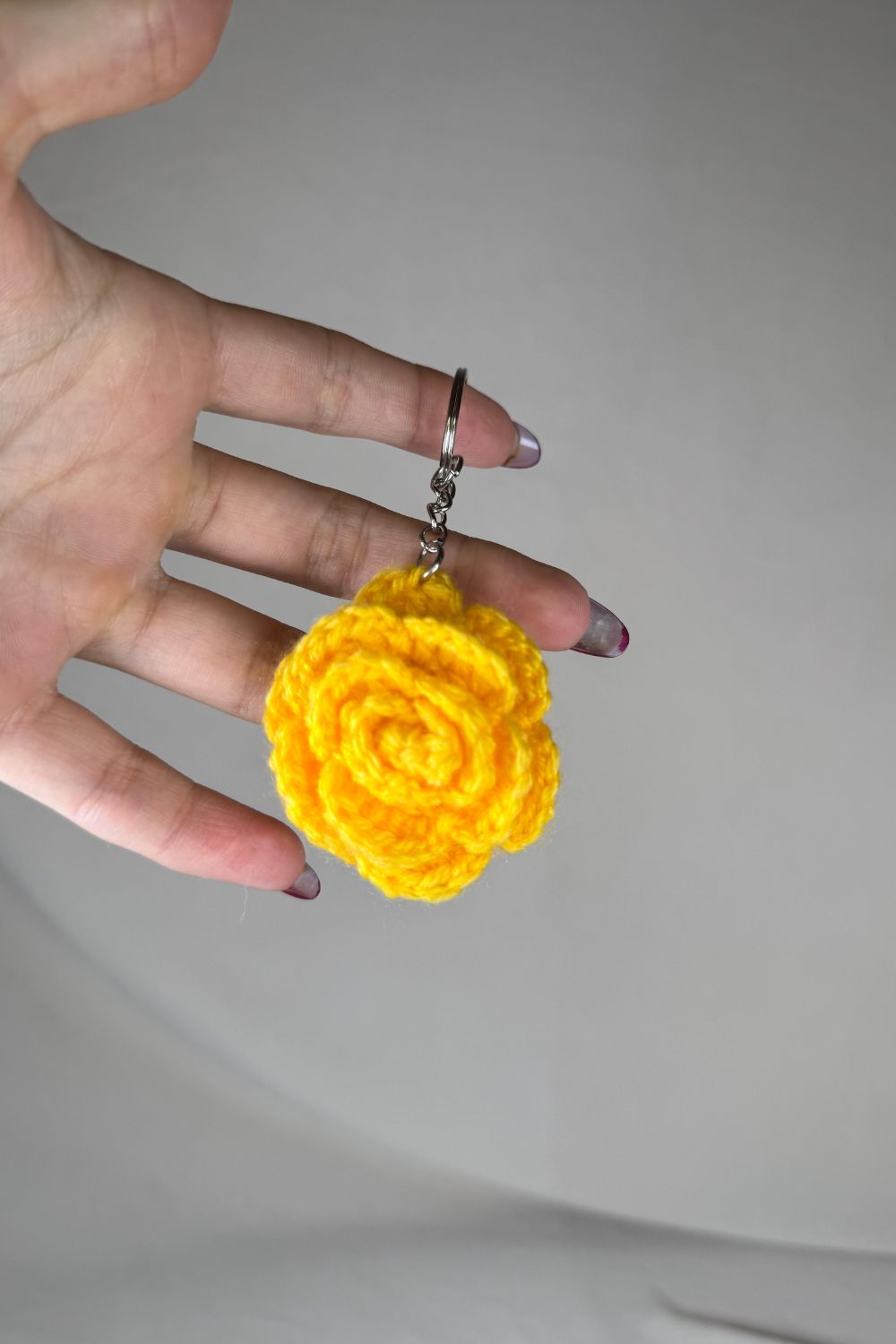 Portachiavi con rosa gialla fatto a mano in Italia da Made By Hand, creazione artigianale in miniatura con fiore rosa all’uncinetto, mostrato in mano per evidenziare i dettagli e le dimensioni