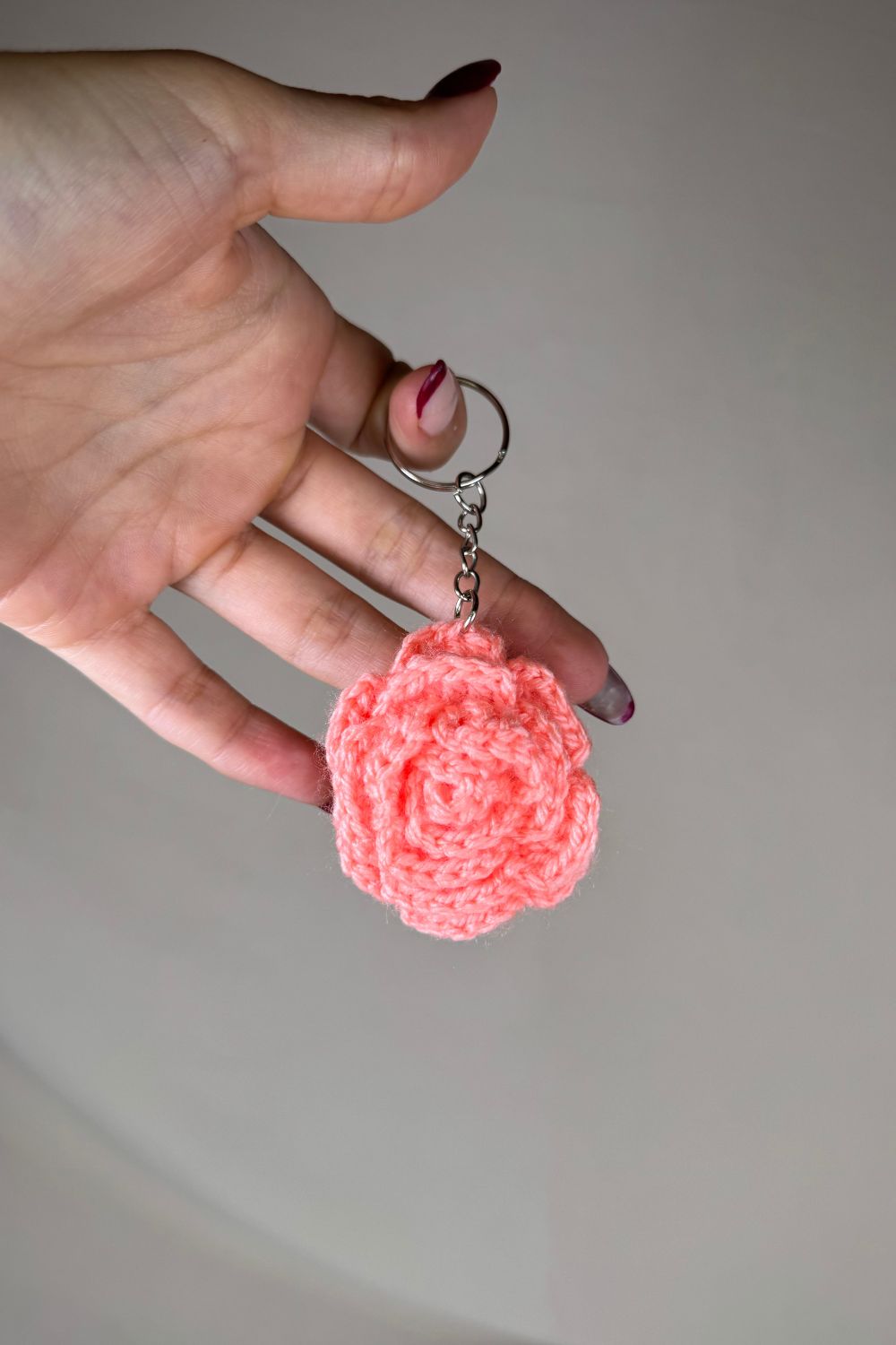Portachiavi con rosa rosa-salmone fatto a mano in Italia da Made By Hand, creazione artigianale in miniatura con fiore rosa all’uncinetto, mostrato in mano per evidenziare i dettagli e le dimensioni