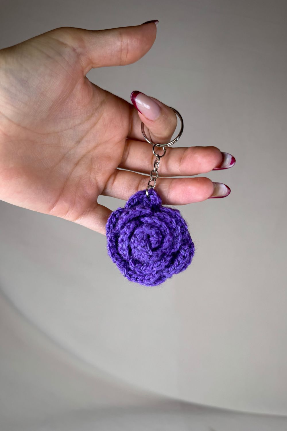 Portachiavi con rosa viola fatto a mano in Italia da Made By Hand, creazione artigianale in miniatura con fiore rosa all’uncinetto, mostrato in mano per evidenziare i dettagli e le dimensioni