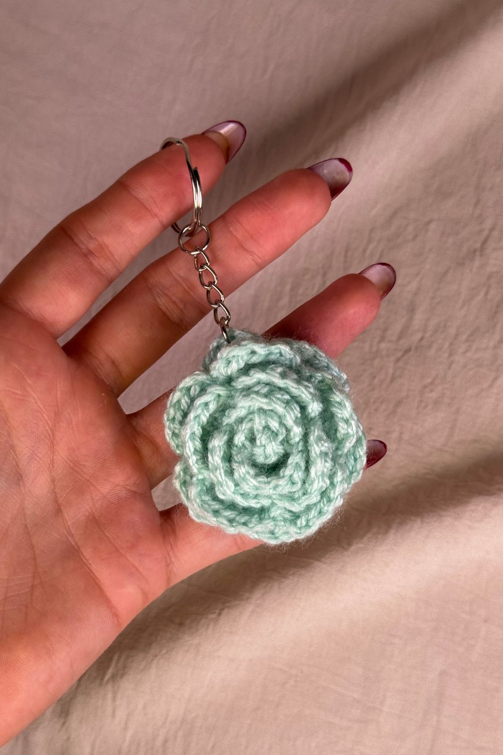 Portachiavi con rosa verde-tiffany fatto a mano in Italia da Made By Hand, creazione artigianale in miniatura con fiore rosa all’uncinetto, mostrato in mano per evidenziare i dettagli e le dimensioni